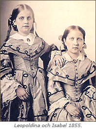 Foto av Leopoldina och Isabel i halvfigur. Leopoldina står lite bakom Isabel med handen på Isabels axel. isabel sitter ner. Båda har fina klänningar på sig med spetsar från armbågen till handleden.