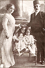 Foto av Huda i tjusig klänning med hennes man, där de står på var sida om en stol och i den sitter två barn, en flicka och en pojke