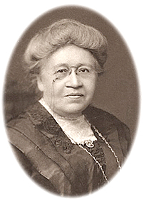 Porträttfoto av Charlotte Yhlen på äldre dar iförd monokel och vacker klänning med spetskrage
