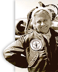 Foto av äldre Jackie Cochran, skrattande framför sitt plan. Införd flygaruniform och mössa.