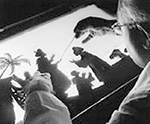 Skarpt beskuren svartvit närbild av Lotte Reiniger vid siluettbordet. Några personer syns i och med att ljuset kommer underifrån. 