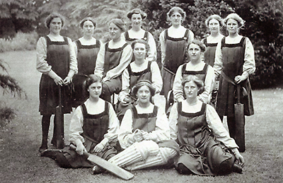 Gruppbild av elever iförda Kingfieldsinstitutets gymnastikdräk med kjolar som slutar vid knäna. Tre flickor sitter på marken som är gräsbeklädd, två sitter på en bänk bakom dem, och sju stycken står bakom dem. 