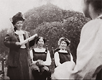 Foto av Martina Bergman Österberg till höger i bild. Hon håller tal för sina elever varav två sitter snett bakom henne och en syns i närbild till höger.