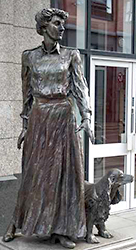 Foto av en staty i helfigur av Constance Markeivicz med en hund