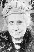 Porträttbild av Célie Brunius i hatt,  cirka 85 år gammal. Hon har kort vitt hår och ser rakt in i kameran