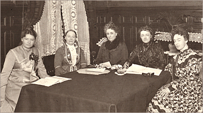 Foto av fem kvinnor sittande runt ett bord med papper liggande framför sig på bordet. Alla ser in i kameran