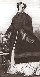 Foto av en kvinna i helfigur iförd en lång kappa över en klänning med krinolin