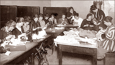 Foto av fjorton kvinnor som sitter runt ett antal bord och syr-