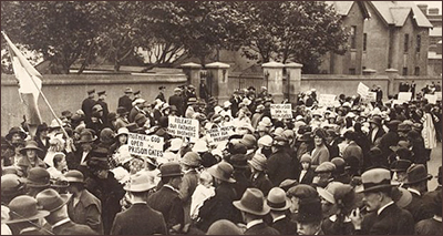Foto av väldigt stor folksamling framför stenmurar. De har plakat med texter som "Mother of God - Open the Prison Gates", "Release our faters and brothers" och "Mother of Mercy - Pray for the Prisoners". Till vänster mitt i massan håller någon i en stor irländsk flagga. En del kvinnro har barn med sig i demonstrationen, och även män deltar.