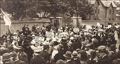 Foto av väldigt stor folksamling framför stenmurar. De har plakat med texter som "Mother of God - Open the Prison  Gates", "Release our faters and brothers" och "Mother of Mercy - Pray for the Prisoners". Till vänster mitt i massan håller någon i en stor irländsk flagga. En del kvinnro har barn med sig i demonstrationen, och även män deltar.