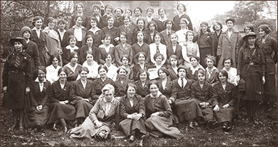 Foto av en stor grupp kvinnor som sitter och står i flera rader på en gräsmatta utomhus