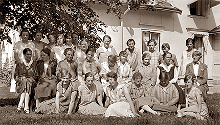 Sommarkursen samlad utanför skolhuset. Kvinnor som står, sitter på stolar och sitter i gräset som i tre rader.