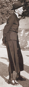 Foto av Elizabeth Tamm i profil och helfigur, stående utomhus iförd hatt
