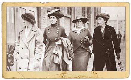 Foto på en pappersram av fyra kvinnor som går i bredd på en gata, de har hattar och kappor på sig