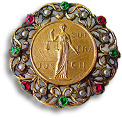 IWSA-broschy i filigran med vita, röda och gröna pärlor, i mitten IWSA:s logotyp med Justitia i soluppgången och texten JUS SUF FRA GII