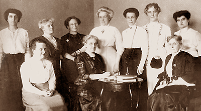 Foto av tre sittande och sju stående kvinnor. I mitten sitter Carrie Chapman Catt vid ett litet runt bord
