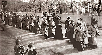 Foto av massor av kvinnor som går i etyt demonstrationståg. Längst fram syns två småflickor gå bredvid tåget.
