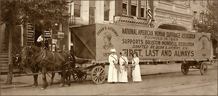 Foto av en stor och lång vagn dragen av två hästar. Framför vagnen står tre kvinnor klädda i vitt. På vagnens sida finns foton av Susan B. Anthony och Anna Howard Shaw till texten: NAWSA Founded in 1869, Supports Briston-Mondell resolution, drafted ny Susan B. Anthony, 1874, First, Last and Always