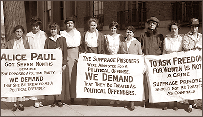 Foto av tio kvinnor som står utomhus och håller upp tre danderoller. På dem står krav på att Alice Paul och andra måste släppas och att de kräver att rösträttsfångarna  ska behandlas som politiska fångar samt att "To Ask for Freedom för Women is Not a Crime".