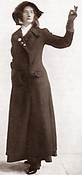 Foto av kvinna i en lång kappa och enkel hatt, hon håller upp ena handen