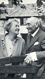 Foto av Emmeline och Frederick i halvfigur, stående vid en grind framför ett hus, de ser kärleksfullt på varandra och ler