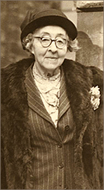 Foto i halvfigur av Mary Sheepshanks på äldre dar, i hatt och päls med glasögon