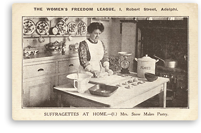 Foto av en suffragett som iförd förkläde bakar. På bordet där hon jobbar finns en våg och diverse hushållssaker du behöver till bak. Bakom henne syns hyllor med en vacker servis och till höger i bilden syns en stor vedspis. Under bilden står förutom rubriken: (1.) Mrs. Snow Makes Pastry.
