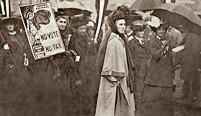 Foto av mörkklädda kvinnor i ett demonstrationståg, många har paraplyer uppfällda. Till vänster syår en som håller i ett plakat med texten "No Vote - No tax". Mitt i bilden en kvinna i ljusare kappa.