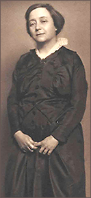 Nästan helfigursbild av Anna Lindhagen när hon är lite yngre, med en mörk klänning med ljus krage