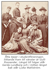 Foto av 5 kvinnor som står och 3 som sitter på golvet. Alla är iförda långa klänningar. Flera bär hatt.