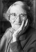 Porträttfoto av Nelly Thüring på äldre dar iförd glasögon. Hon lutar huvud i ena handen