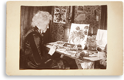Foto av Matilda framför ett bord  som det ligger akvarellfärger och målningar av blommor på