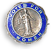 Gammaldags rockmärke med texten Votes for Women i silver mot blå botten runt en typisk fru Justitia