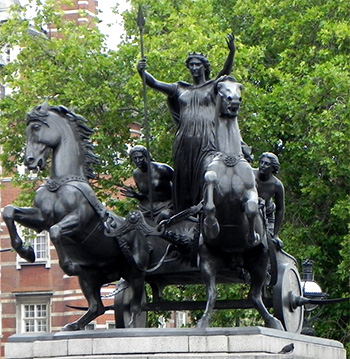 Foto av staty av drottning med armarna lyfta och ett spkut i handen. Hon rider på en vagn dragen av hästar som stegrar sig. Bakom henne står två unga kvinnor