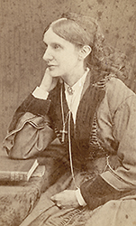 Foto av Josephine Butler i halvfigor, sittande framför ett bors med en bok, hon ser åt sidan
