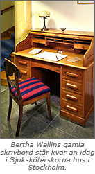 Foto av ett gammaldags skrivbord med lådor och fack, tillsammans med texten "Bertha Wellins gamla skrivbord står kvar än idag i Sjuksköterskornas hus i Stockholm"