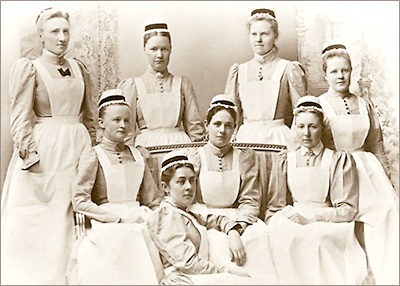 Foto av åtta Sophiasystrar i uniform, fyra står och fyra sitter. På huvuden har de en hätta och håret stramt uppsatt.