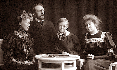 Familjefoto med en mamma, en pappa och två barn som sitter runt ett bord. Barnen ser in i kameran