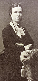 Foto av Johanna Hedén i halvfigur. Hon lutar sig mot en fåtölj och ser rakt in i kameran