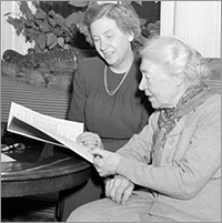 Foto av Signe och Kerstin sittande vid ett bord, de bläddrar i en tidskrift och ser ner mot den