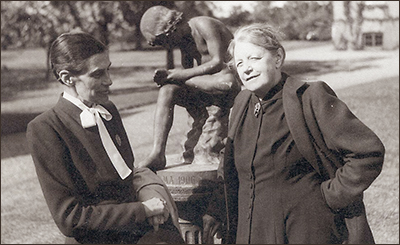 Foto i halvfigur av Honorine Hermelin och Ada Nilsson som står utomhus framför en staty