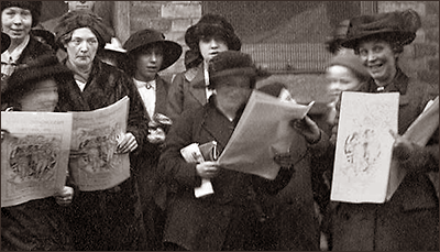 Delvis suffigt foto av omkring tio kvinnor som alla står med tidningen Woman's Dreadnought i händerna. Några skrattar eller ler.