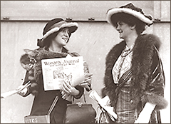 Foto av två kvinnor som står utomhus och pratar. Den till vänster håller i flera exemplar av tidningen "Women's Journal".