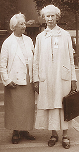 Foto av Augspurg och Heymann i helfigur på äldre dar. Heymann bär på en portfölj och ser in i kameran. Augspurt ser på Heymann
