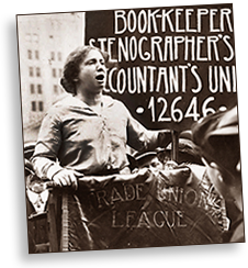Foto av Rose Schneiderman som håller tal. Hon håller i sig i ett podie som har ett tyg hängande, där det står något som slutar med "Trade Union League" I bakgrunden står en skylt eller något som börjar med texten Book-keeper, Stenographer's.