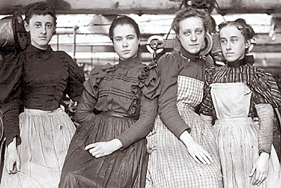 Foto av fyra amerikanska fabriksarbeterskor, två har förkläden på sig. Det går att ana en fabrikslokal i bakgrunden, tre av flickorna ser in i kameran, den fjärde ser åt sidan, de lutar sig emot varandra,