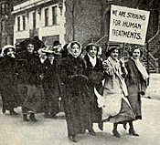 Foto av unga kvinnor i ett demonstrationståg på vintern. Den tredje från vänster av de fyra främsta har ett plakat där det står: We are striking for human treatments.