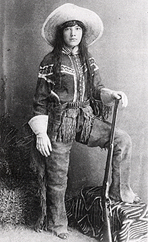 En cowgirl med byxor, handskar och gevär