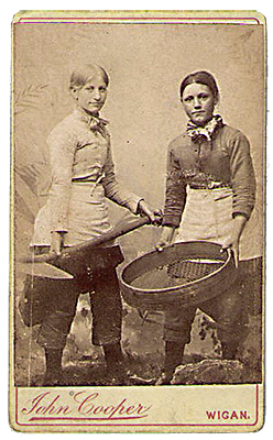Foto av två byxklädda tjejer. En har en spade och en har någon slags stor sil.