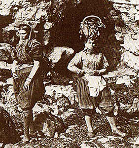 Två kvinnor med korgar pu huvudet och en sorts bloomers på sig framför klippformationer